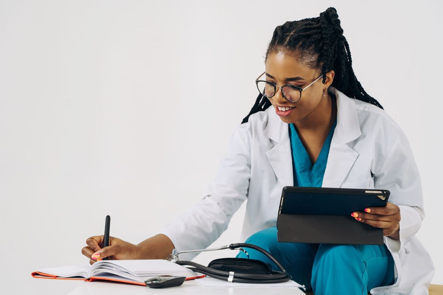 Médica sorrindo, anotando em um caderno e consultando o tablet